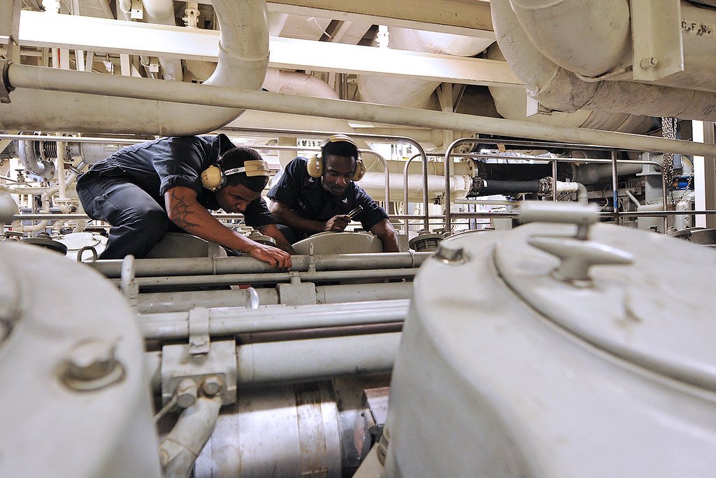 Marine engineers maintaining ship machinery in vessel engine room